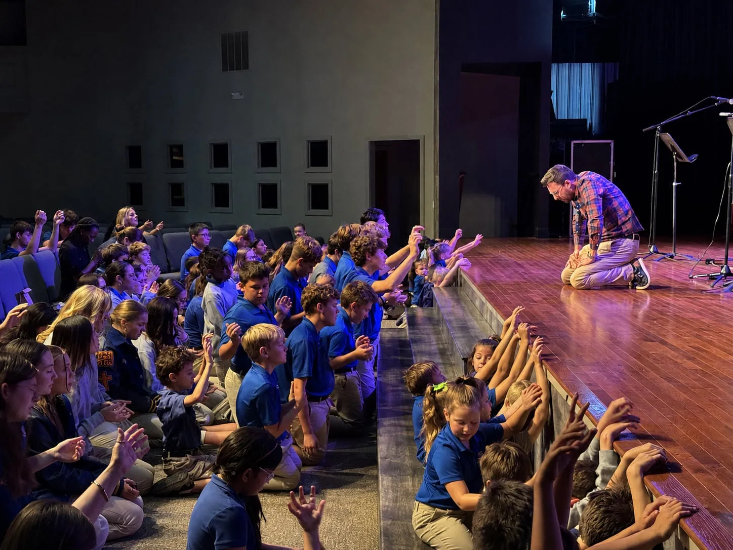 Hill Country Christian School students kneeling in prayer during chapel as a leader prays from the stage